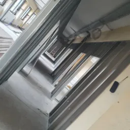 Montaż metalowego stelażu sufitu podwieszanego z płyt kartonowo-gipsowych w korytarzu, widok z dołu na konstrukcję nośną i instalacje elektryczne.