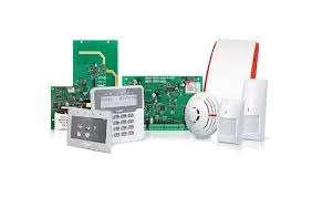 Zestaw komponentów systemu zabezpieczeń: centrala alarmowa z klawiaturą, czujnik dymu, czujnik ruchu i płytki drukowane elektroniki, na białym tle.