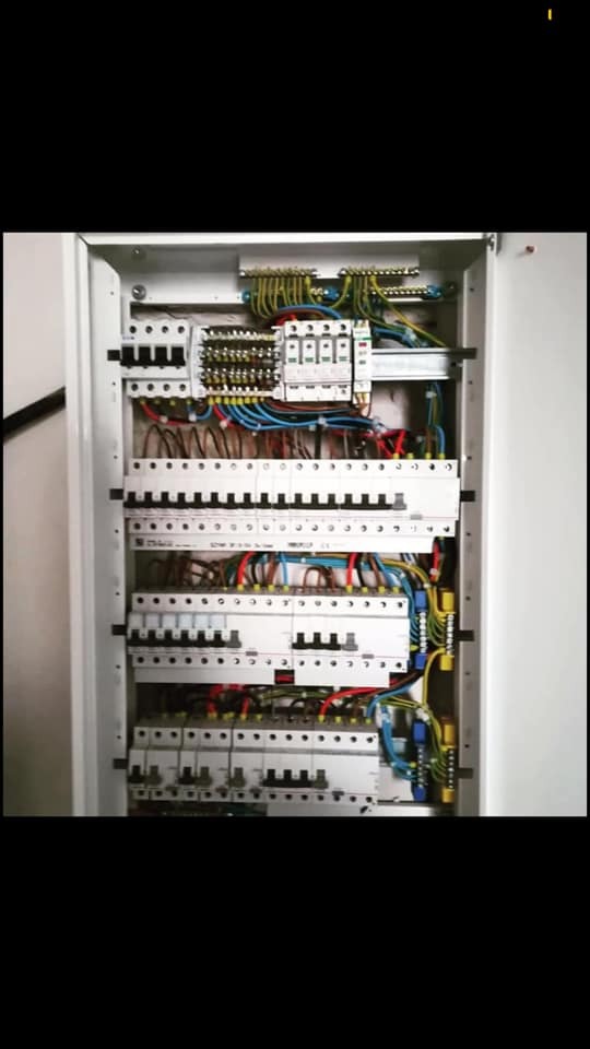 Wnętrze rozdzielnicy elektrycznej z widocznymi bezpiecznikami, przewodami i listwami zaciskowymi, zainstalowanej w białej obudowie.