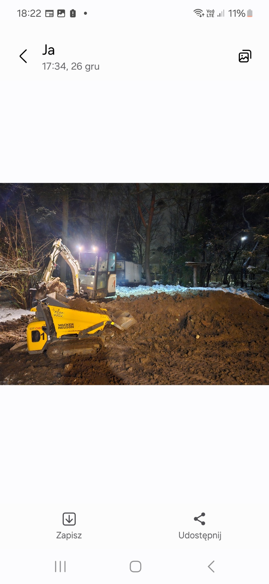 Żółta mini-ładowarka Wacker Neuson DT08 na tle ziemi i drzew w nocy, oświetlona reflektorami, w trakcie prac ziemnych.