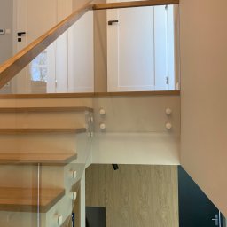 Nie Do Zbicia - Szklana balustrada z drewnianą poręczą, zamontowana na schodach w Piastowie. Nowoczesny design, jasne wnętrze, widoczne detale mocowania szkła.