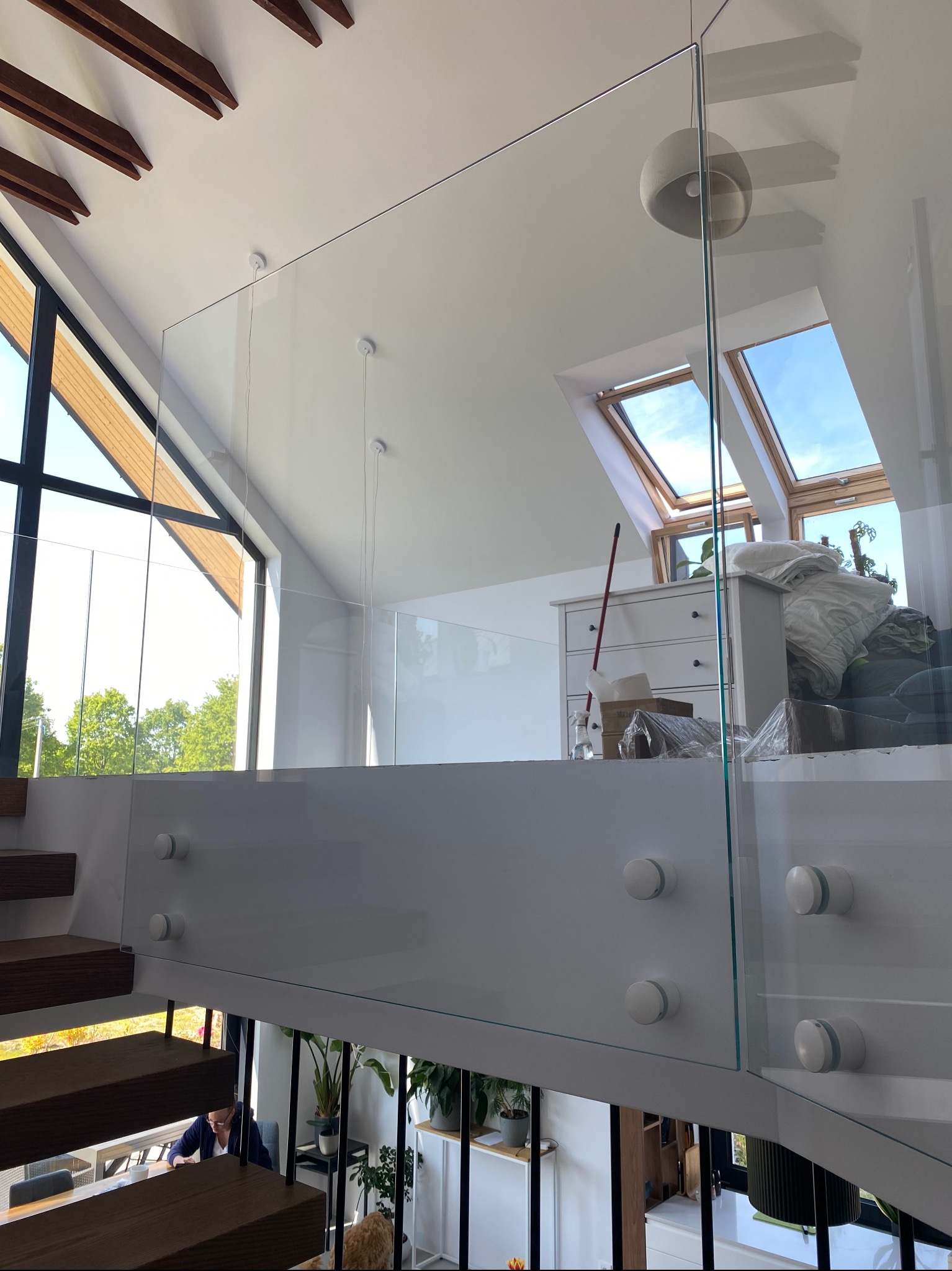 Szklana balustrada z mocowaniami punktowymi w nowoczesnym domu z dużymi oknami i drewnianymi elementami. Widok z góry na schody i parter.