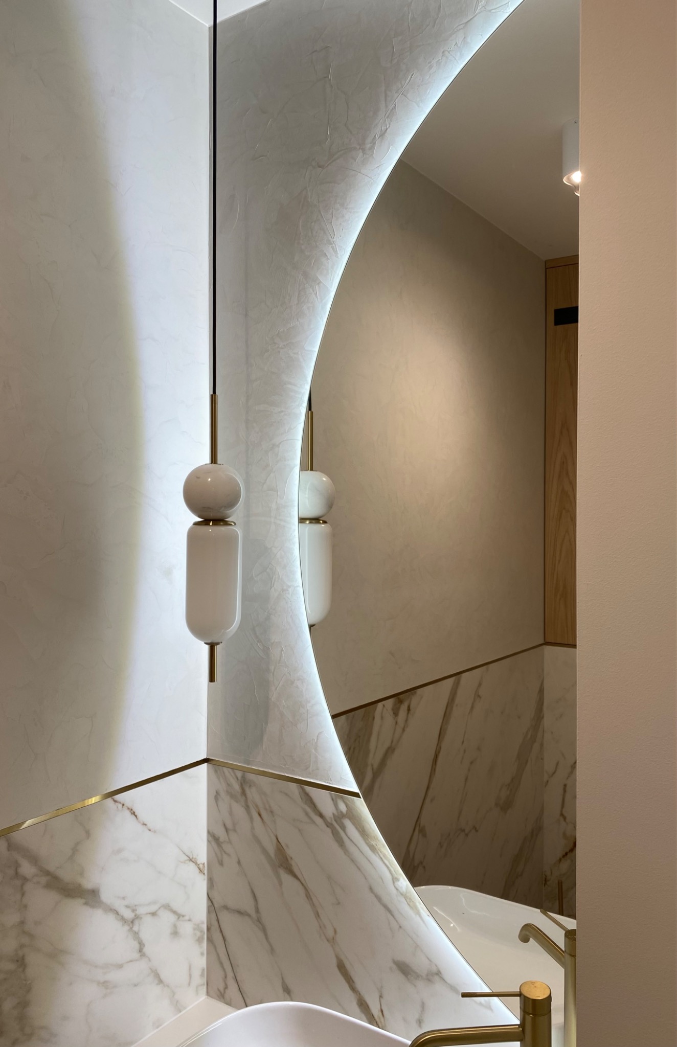 Okrągłe lustro z podświetleniem LED w nowoczesnej łazience z marmurowymi płytkami i złotą armaturą, odbijające minimalistyczną lampę.