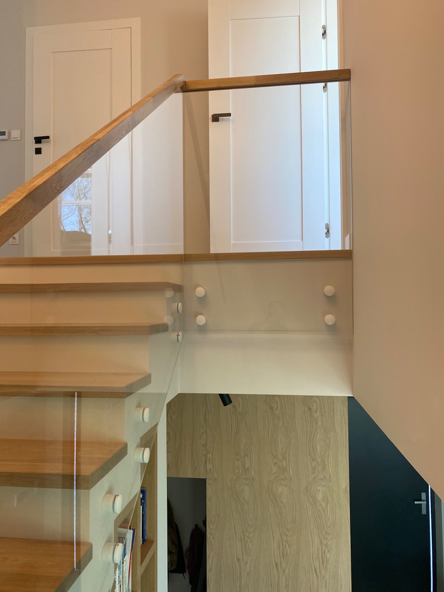 Szklana balustrada z drewnianą poręczą, zamontowana na schodach w Piastowie. Nowoczesny design, jasne wnętrze, widoczne detale mocowania szkła.