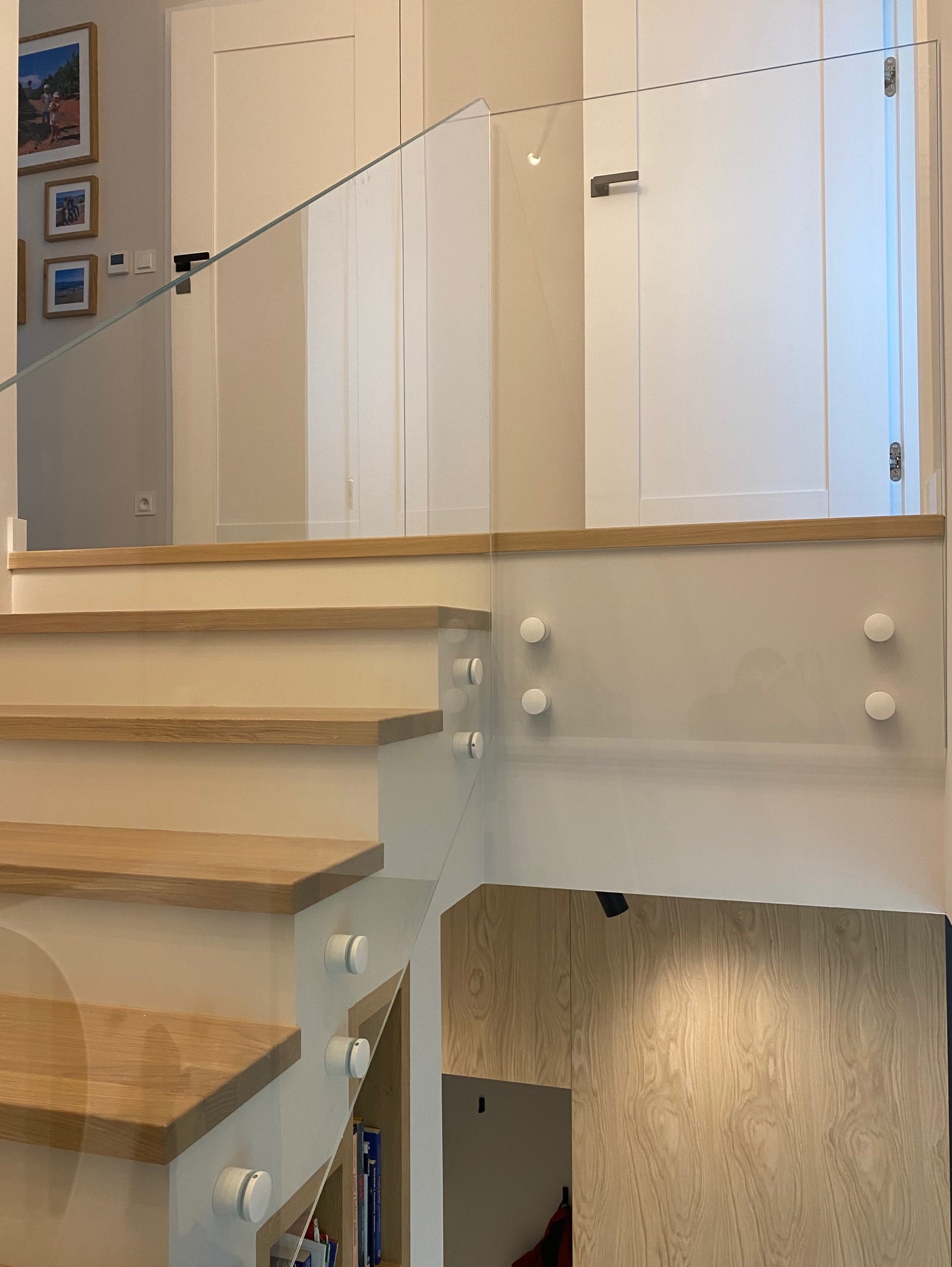 Nowoczesna szklana balustrada mocowana punktowo na schodach z drewnianymi stopniami. Minimalistyczny design, jasne wnętrze.