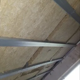 Izolacja poddasza wełną mineralną zamocowaną pomiędzy metalowymi profilami, widoczne okno dachowe.