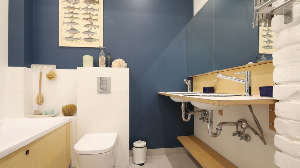 Nowoczesna łazienka z granatową ścianą, dwiema umywalkami na drewnianym blacie, białą cegłą i akcesoriami, takimi jak gąbki i szczotka do ciała.