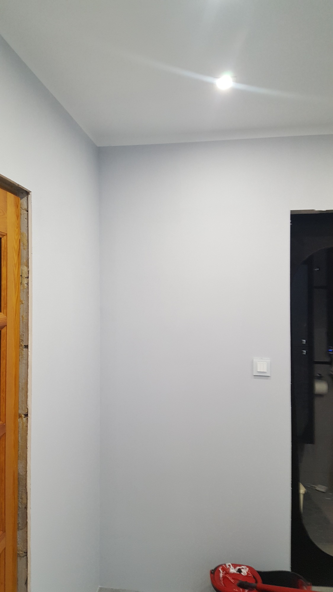 Świeżo pomalowane na szaro ściany w pomieszczeniu w Kaliszu Pomorskim, widoczny fragment futryny drzwi i włącznik światła, na podłodze czerwone wiadro z farbą.
