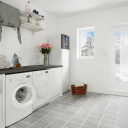 Nowoczesna pralnia z białą zabudową, pralkami Electrolux, szarą podłogą z płytek, pompą ciepła Daikin, świeżymi różami w wazonie i widokiem na zimowy krajobraz za oknem.