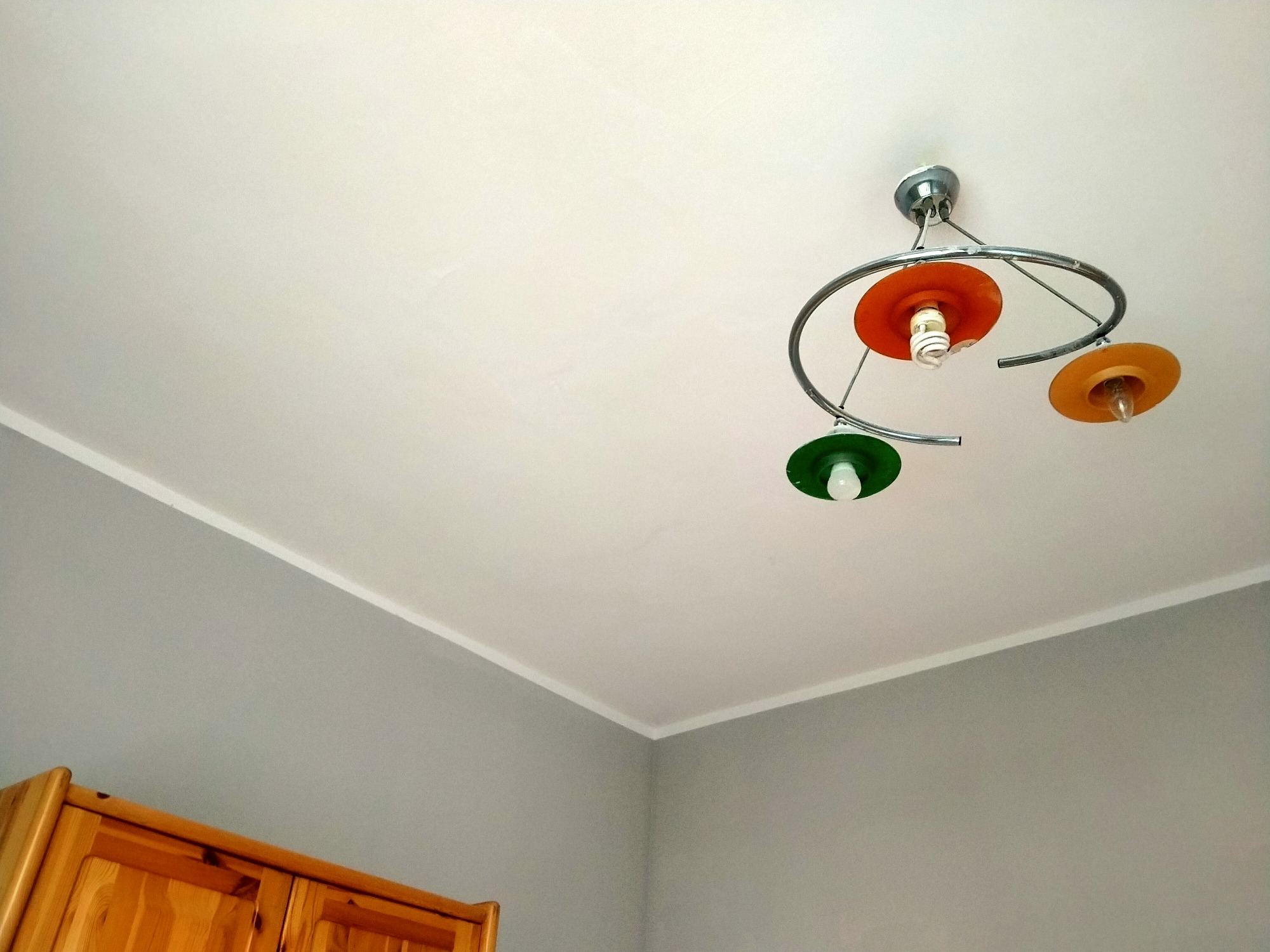 Świeżo pomalowany szary pokój w Gliwicach z widoczną drewnianą szafką i nowoczesną lampą sufitową z kolorowymi kloszami.