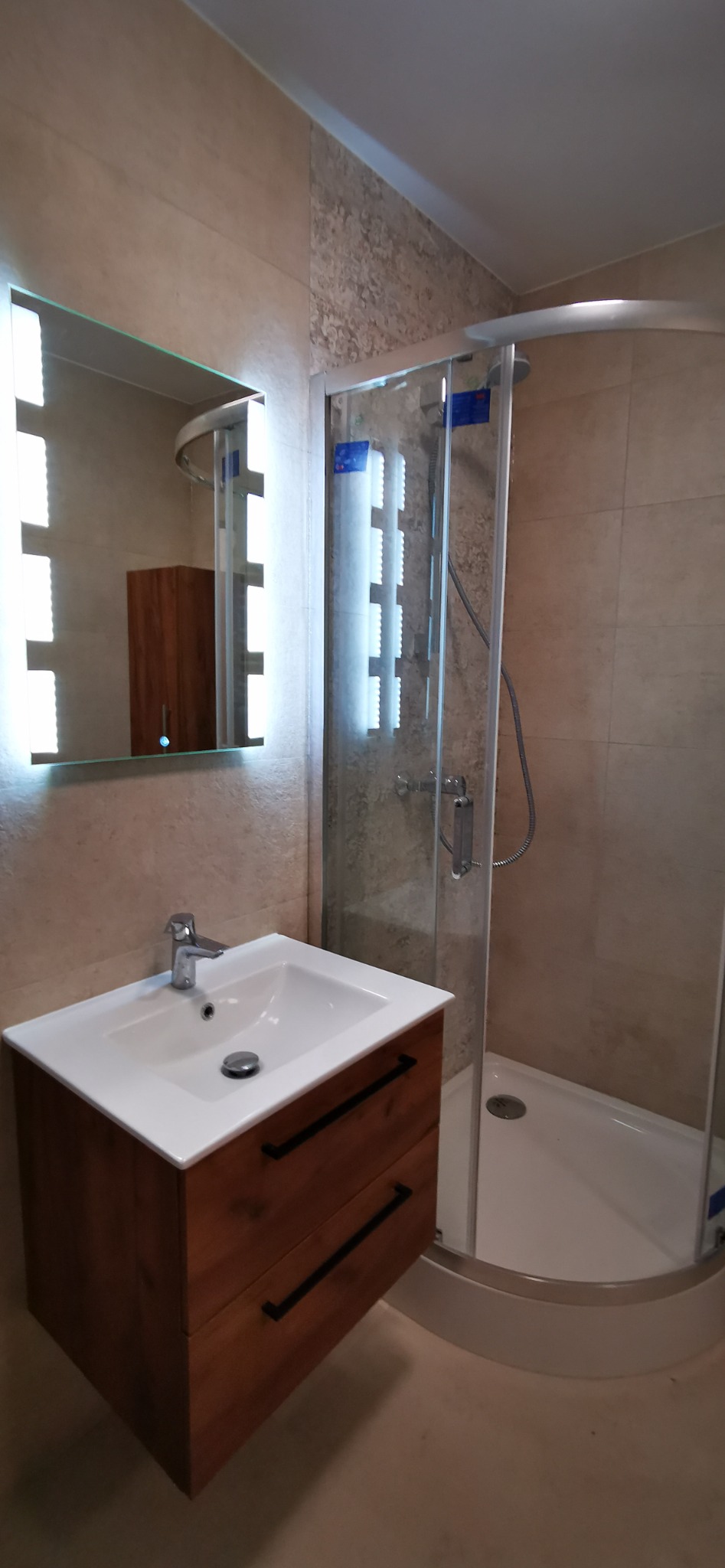 Nowoczesna łazienka z kabiną prysznicową z zaokrąglonymi szybami, umywalką nablatową na szafce z ciemnego drewna oraz lustrem z podświetleniem LED.