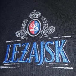 Czarna koszulka polo z wyhaftowanym niebiesko-białym napisem 'LEZAJSK' i herbem z koroną w kolorach czerwonym i niebieskim.