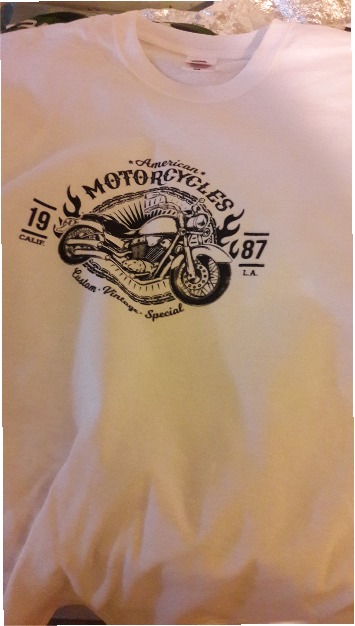 Biała koszulka z nadrukiem czarnego motocykla w stylu vintage z napisem 'American Motorcycles 1987 Calif. L.A. Custom Vintage Special'.
