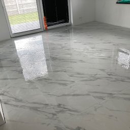 WASBUD Maciej Wąsiewski - Błyszcząca, biała podłoga wyłożona płytkami imitującymi marmur, widok z perspektywy podłogi, z oknami w tle