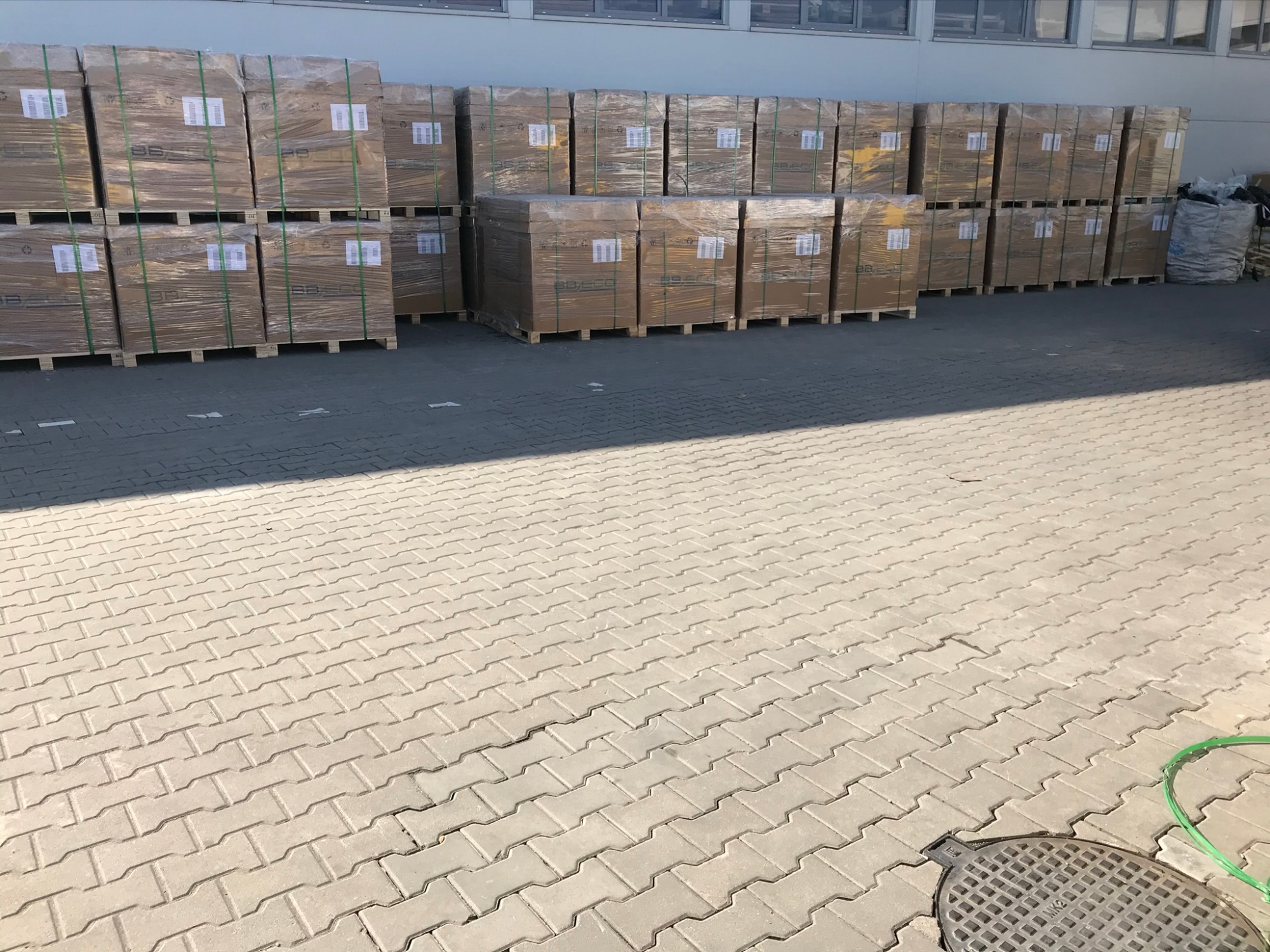 Palety z panelami, prawdopodobnie fotowoltaicznymi, przygotowane do montażu w Warszawie, składowane na zewnątrz budynku.