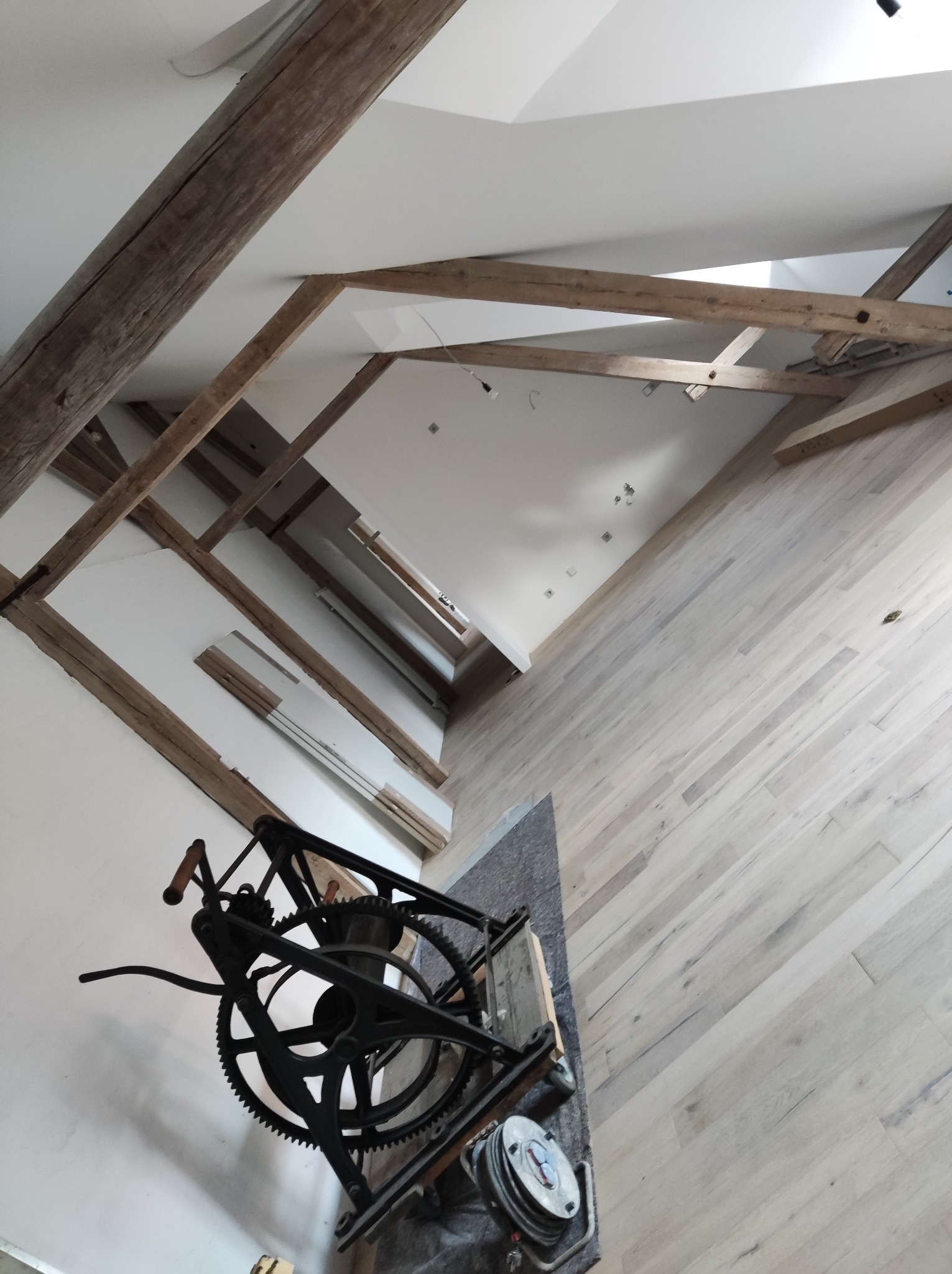 Poddasze po renowacji z widocznymi drewnianymi belkami, nową podłogą z jasnego drewna i sprzętem do obróbki parkietu.