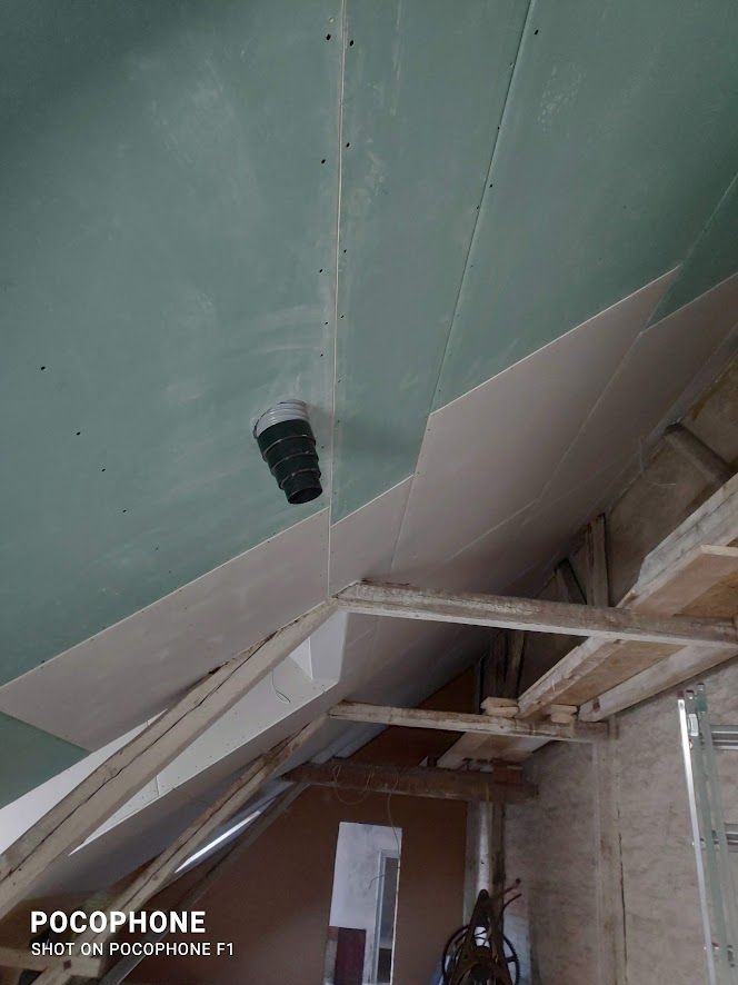 Montaż płyt gipsowo-kartonowych na skośnym poddaszu, widoczne drewniane elementy konstrukcyjne i rura wentylacyjna wystająca z sufitu.