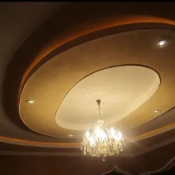 Dekoracyjny sufit z podwieszanym elementem w kształcie elipsy, oświetleniem punktowym i kryształowym żyrandolem, wykończony w odcieniach beżu i brązu.