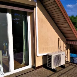 Klimatyzator zewnętrzny marki Sevra zamontowany na balkonie domu z widocznym basenem w tle, z naklejką 'Klimatyzacja Pompy Ciepła RControl' na szybie.