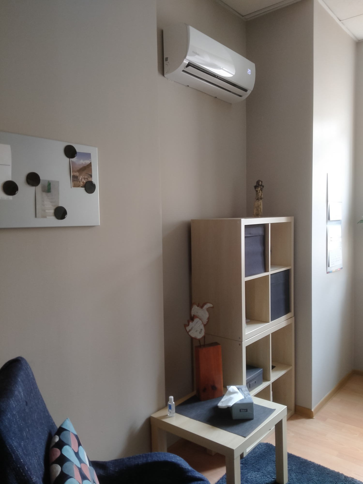 Biały klimatyzator ścienny z wyświetlaczem temperatury 20 stopni Celsjusza, zamontowany w jasnym pokoju z regałem, stolikiem i dekoracjami.