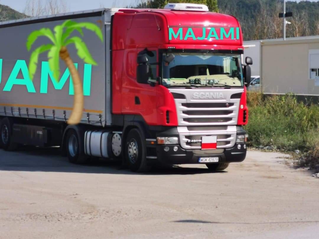 Czerwona ciężarówka Scania z naczepą z napisem 'MAJAMI' i palmą na boku, zaparkowana na placu.