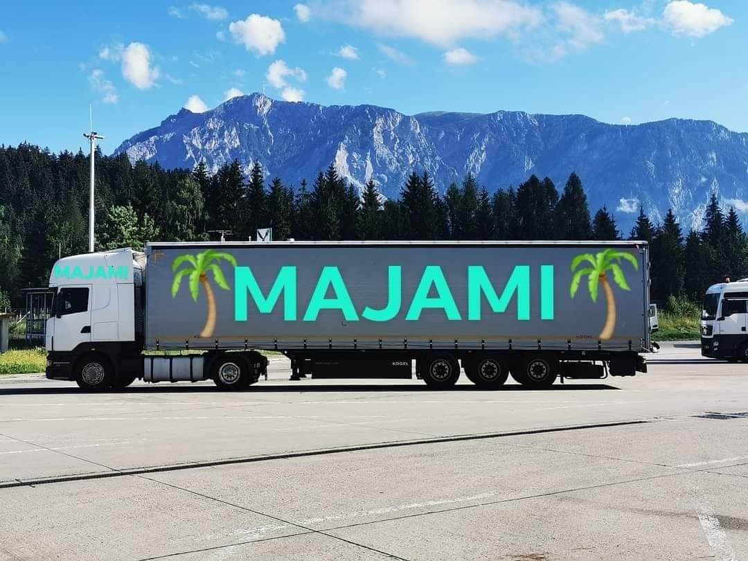 Ciężarówka z naczepą z napisem 'MAJAMI' i palmami na tle górskiego krajobrazu.