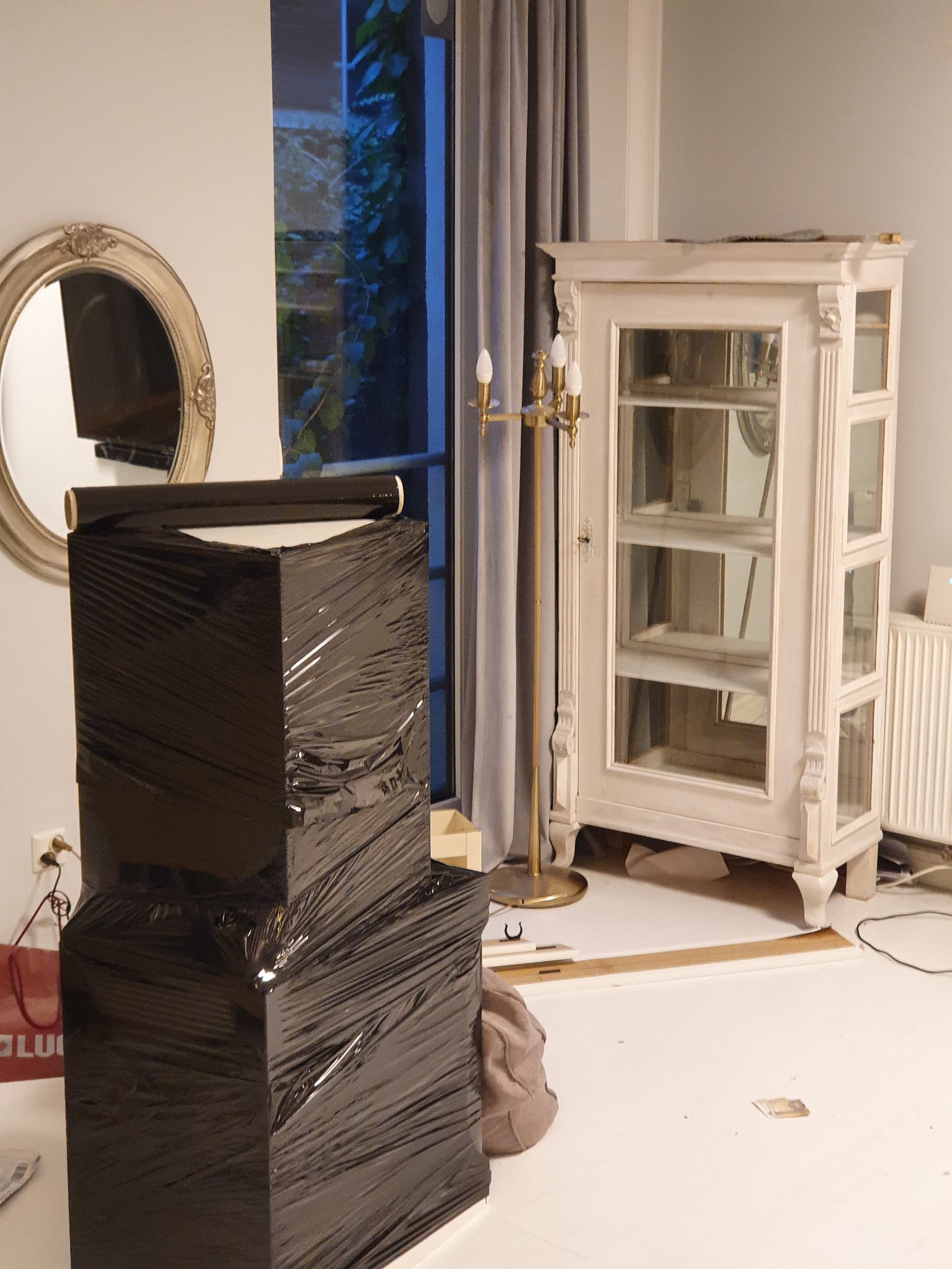 Dwa kartony zabezpieczone czarną folią stretch, gotowe do transportu, obok antyczna witryna i okrągłe lustro w ozdobnej ramie