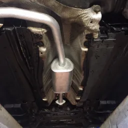 Widok podwozia samochodu z nowym, srebrnym tłumikiem na tle zabezpieczonej termicznie karoserii, po konserwacji antykorozyjnej.