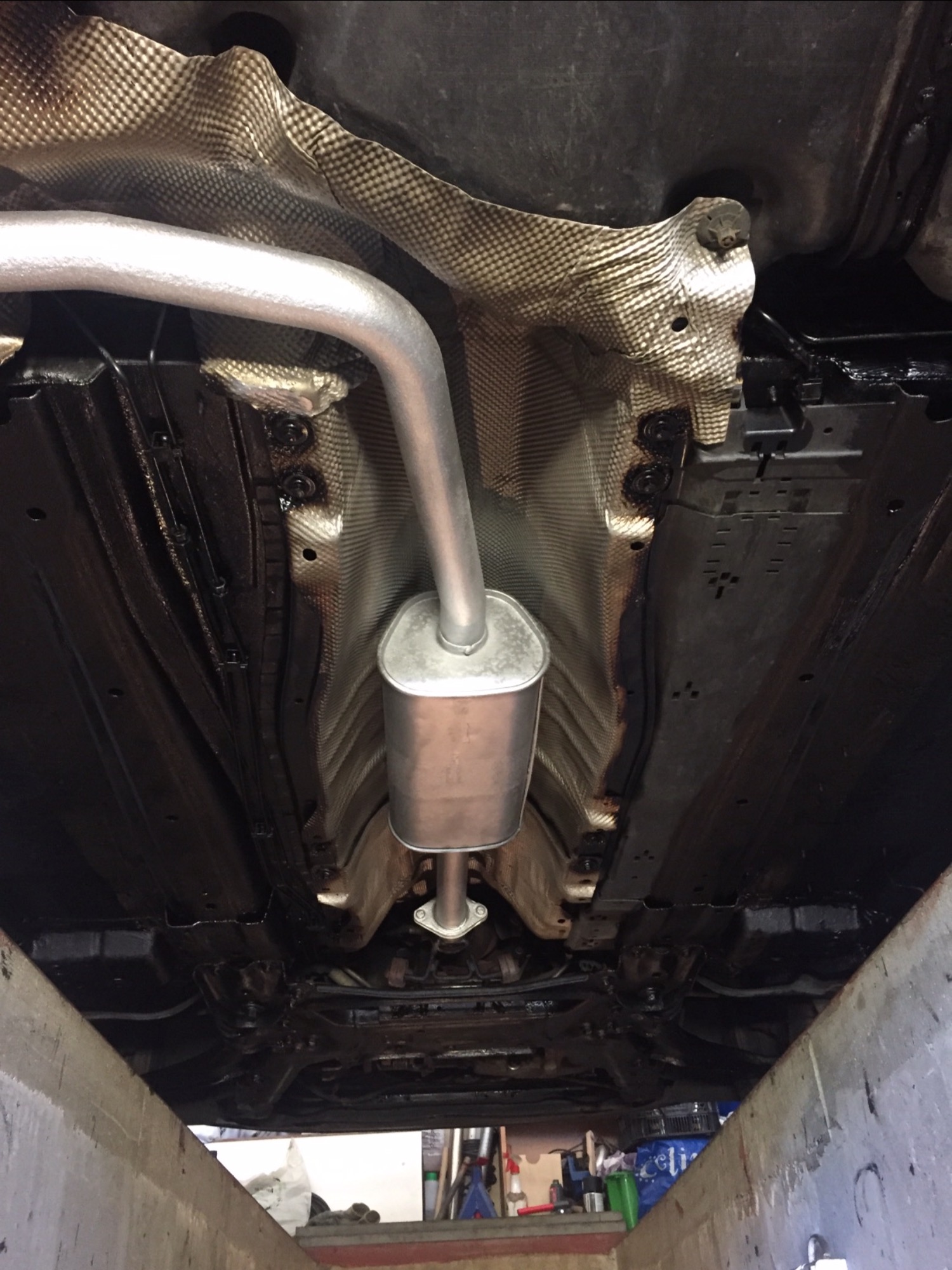 Widok podwozia samochodu z nowym, srebrnym tłumikiem na tle zabezpieczonej termicznie karoserii, po konserwacji antykorozyjnej.