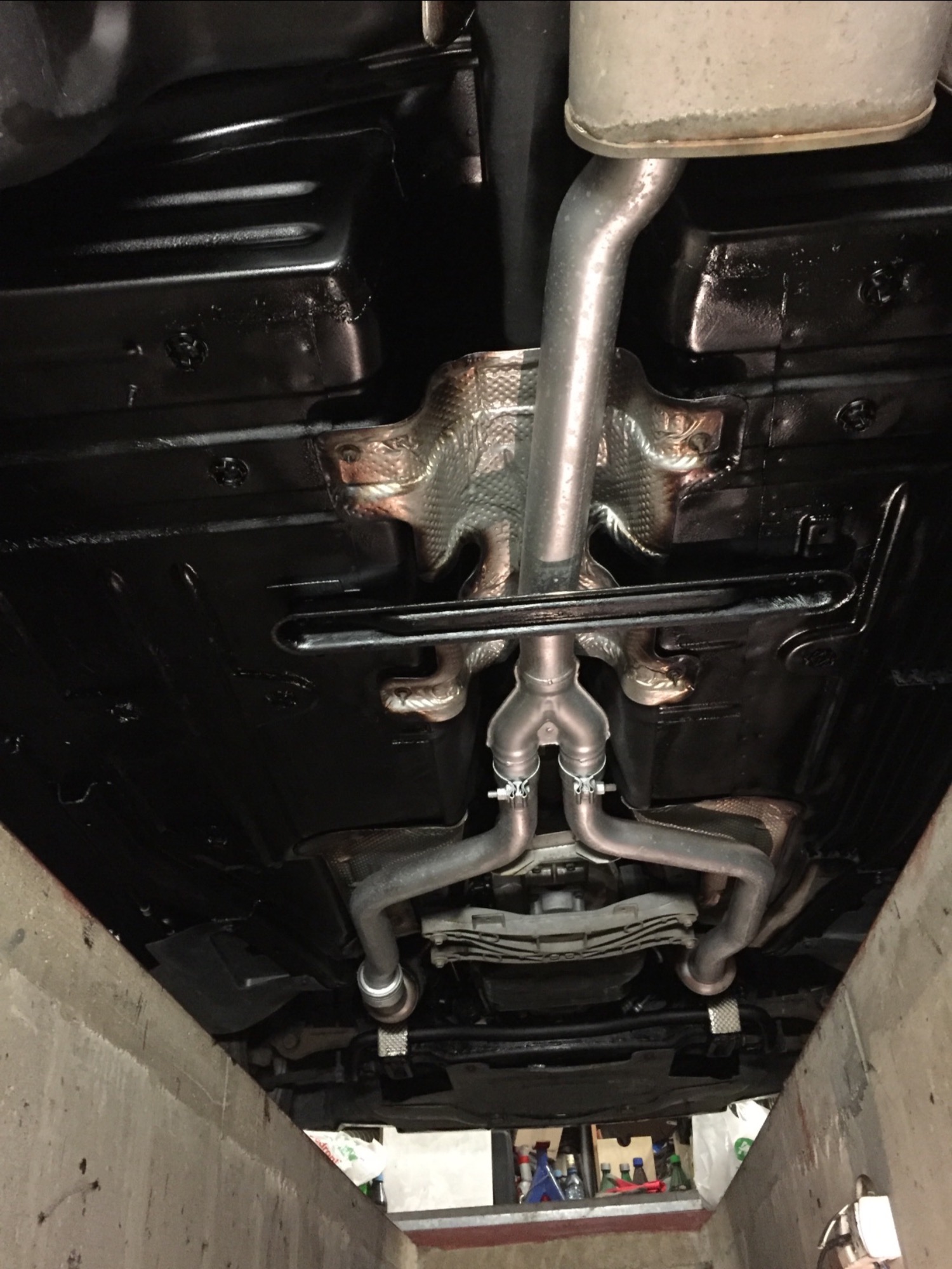 Podwozie samochodu po zabezpieczeniu antykorozyjnym, widoczne elementy układu wydechowego i świeża, czarna powłoka ochronna.