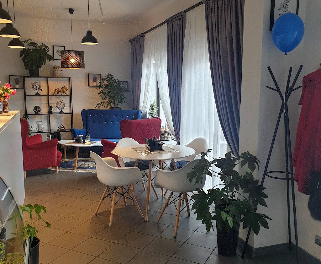 Eleganckie wnętrze kawiarni z zasłonami w odcieniach bieli i szarości, niebieskim balonem i roślinami doniczkowymi.