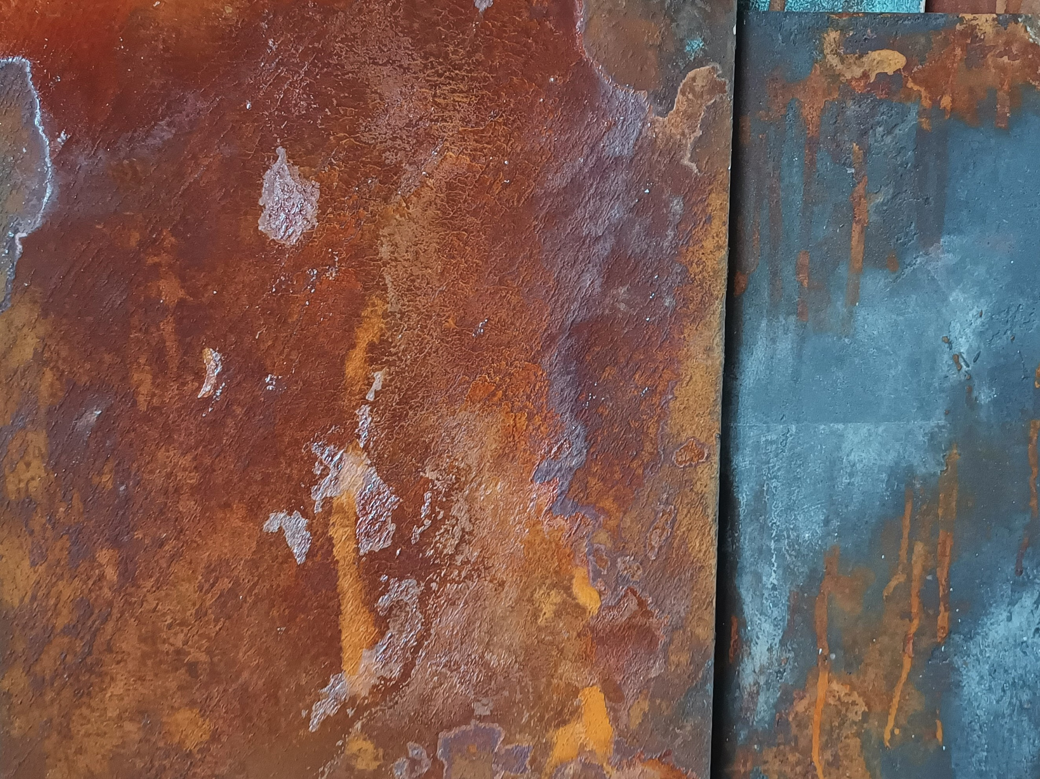 Tekstura rdzawej ściany w Tychach, ukazująca nieregularne wzory i odbarwienia, sąsiadująca z fragmentem ściany w odcieniach szarości z rdzawymi zaciekami.