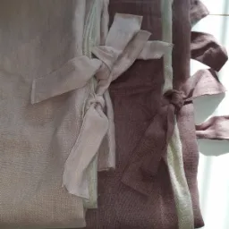 Stos lnianych zasłon w odcieniach różu i brązu, związanych dekoracyjnymi troczkami, z widoczną fakturą tkaniny.