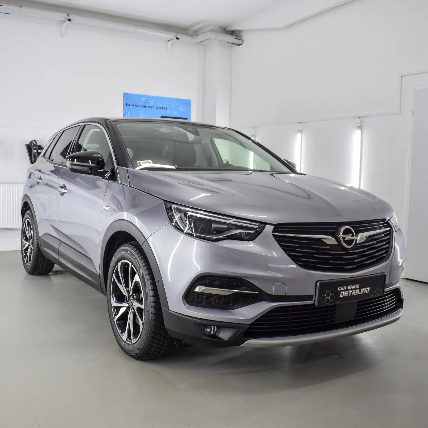Szary Opel Grandland X po zabiegach detailingu, widoczne logo firmy na przednim zderzaku, czyste felgi i lakier, oświetlenie studyjne.