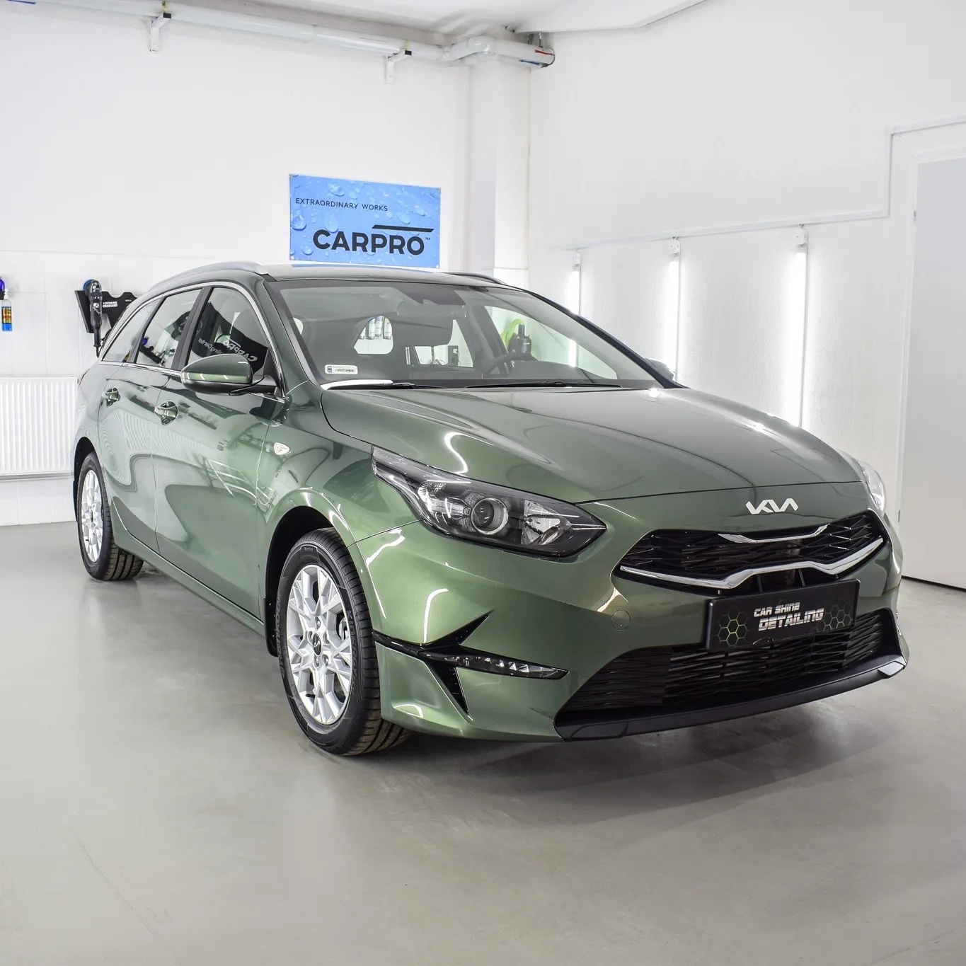 Zielony samochód Kia kombi po detailingu, widoczne logo Car Shine Detailing na przednim zderzaku, czyste felgi i lakier w jasnym pomieszczeniu.