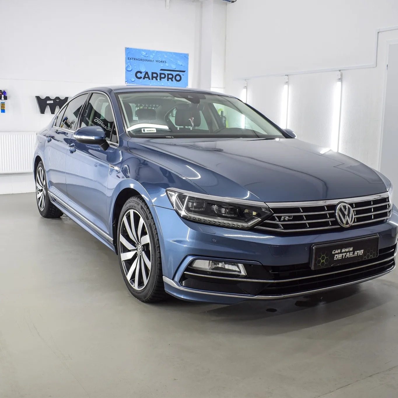 Błękitny Volkswagen Passat po zabiegach pielęgnacyjnych, widoczny w jasnym pomieszczeniu z logo Carpro w tle.