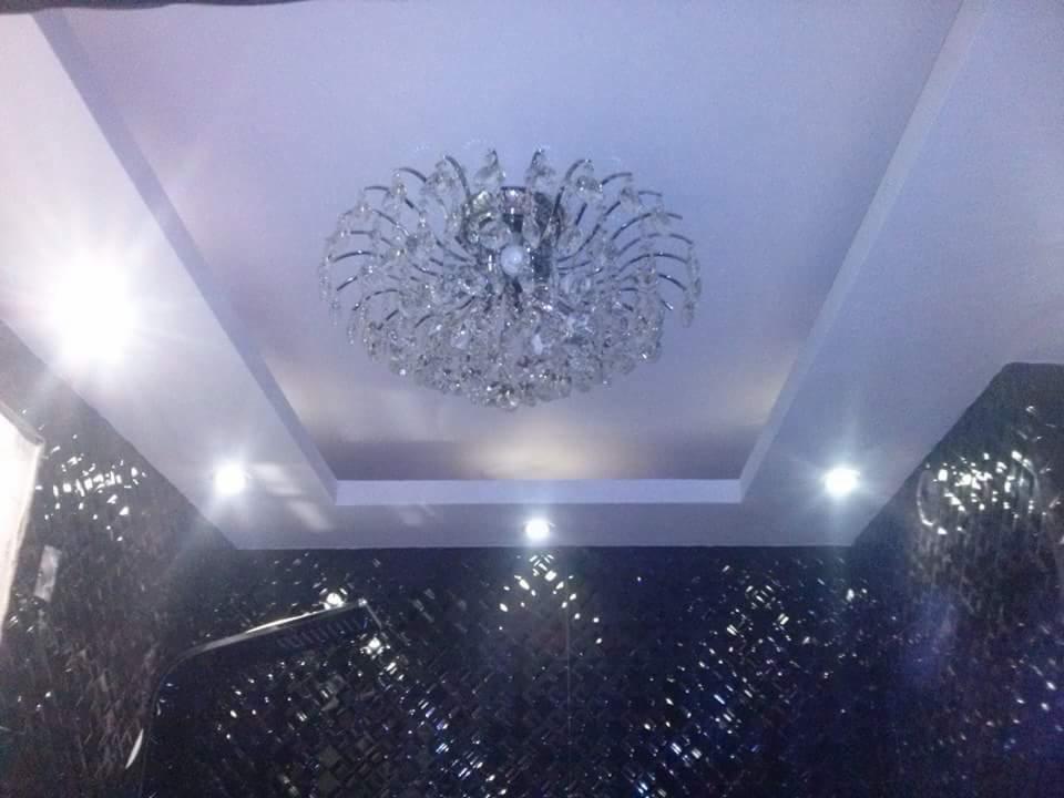 Kryształowy żyrandol w kwadratowej wnęce sufitowej, ciemna ściana z mozaiki lustrzanej odbijająca światło.