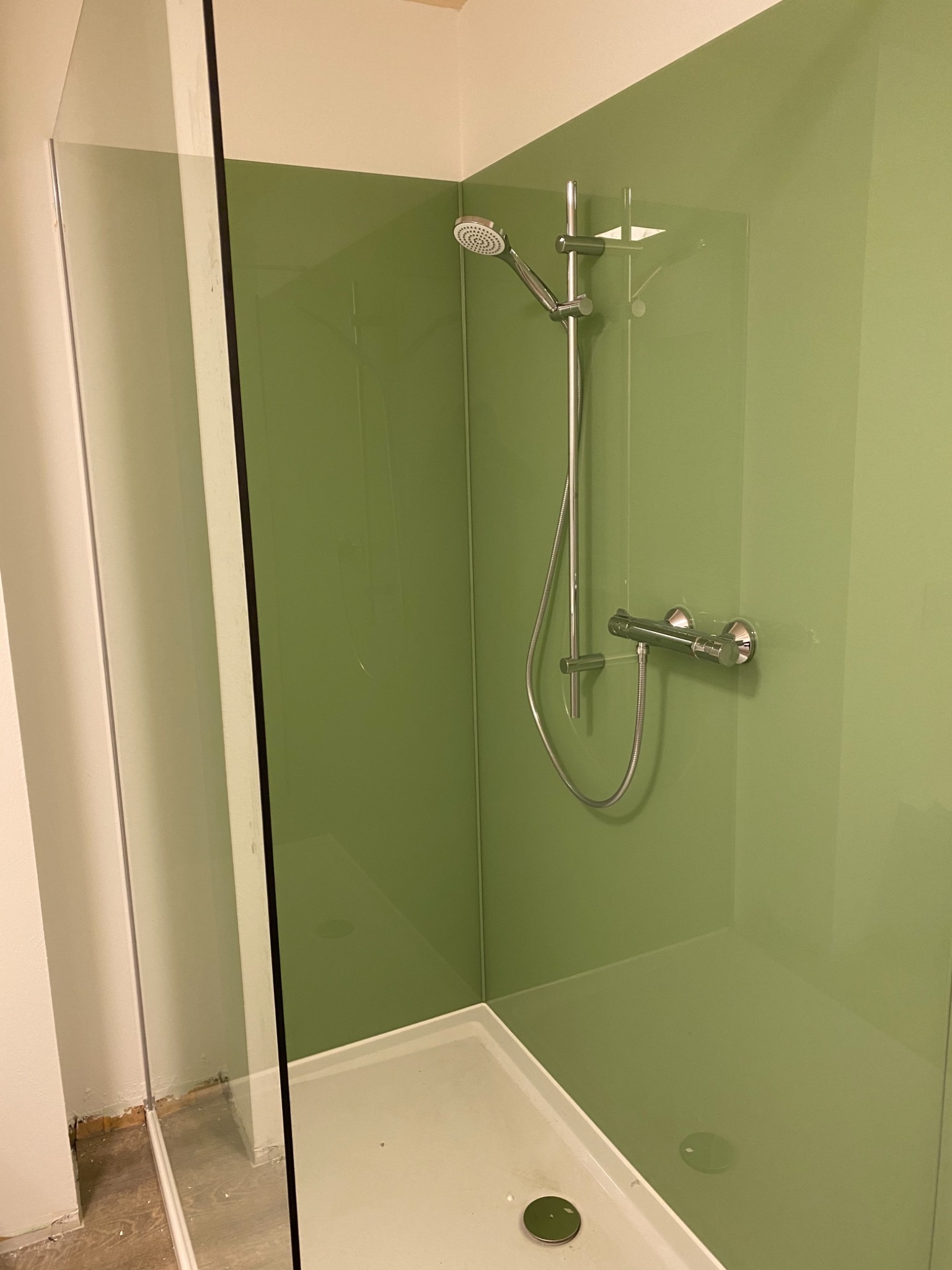 Nowoczesna kabina prysznicowa z zielonymi panelami ściennymi, widoczna chromowana armatura i szklane drzwi w trakcie montażu, z niedokończonym wykończeniem podłogi.