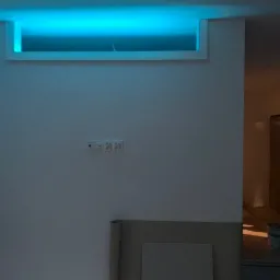 Wnęka sufitowa z podświetleniem LED w kolorze niebieskim, widoczne gniazdka elektryczne na ścianie, remont w trakcie, widoczne wiadra i narzędzia w tle.