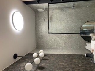 Nowoczesna łazienka z okrągłym oknem z podświetleniem LED, szklaną kabiną prysznicową i dekoracyjną lampą podłogową z kulami.