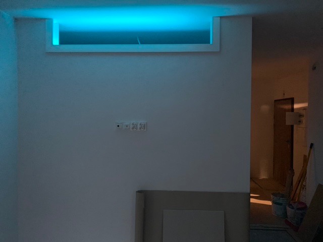 Wnęka sufitowa z podświetleniem LED w kolorze niebieskim, widoczne gniazdka elektryczne na ścianie, remont w trakcie, widoczne wiadra i narzędzia w tle.