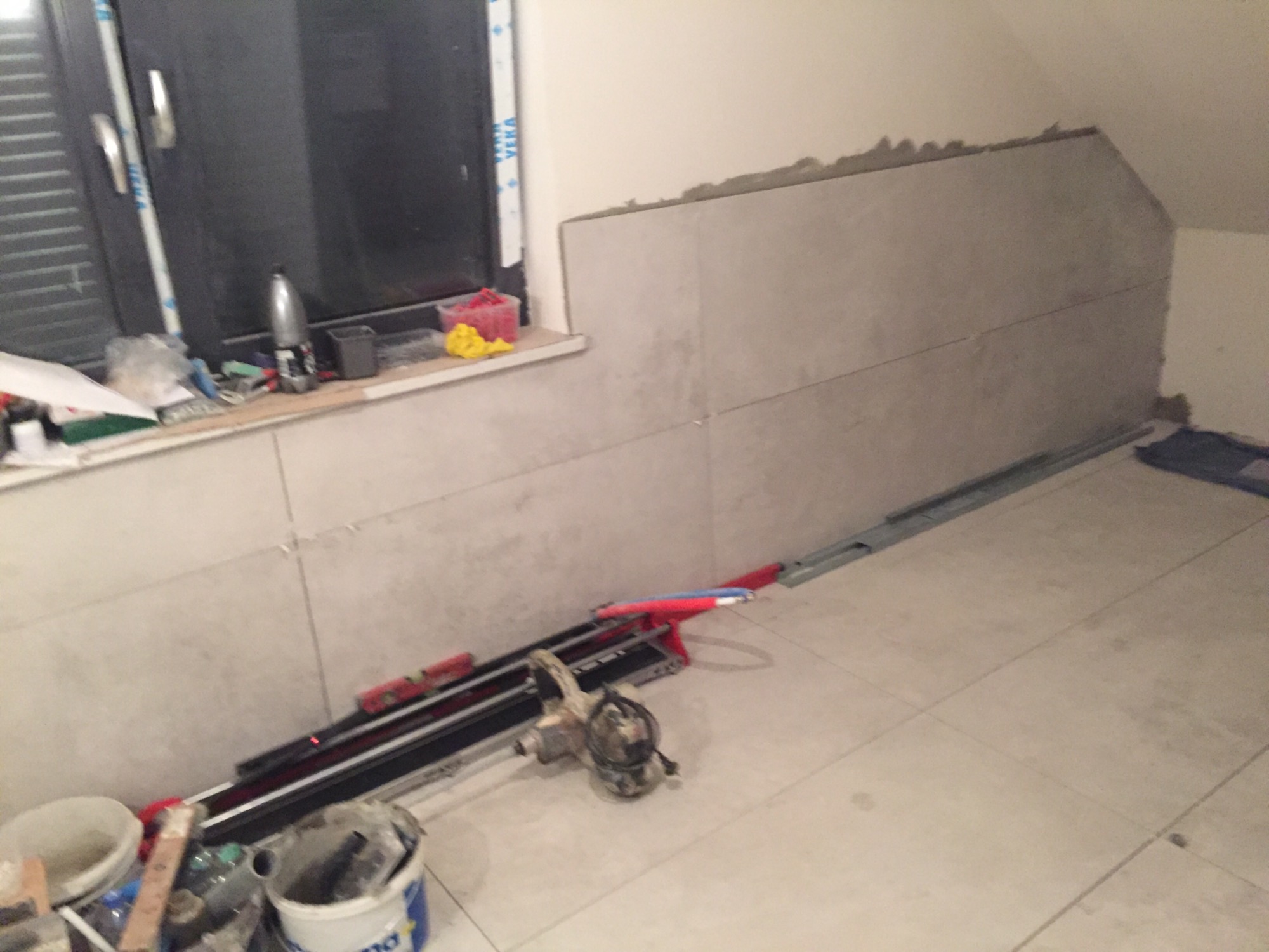 Ściana w trakcie układania płytek w poddaszu, widoczna przymiarka płytek pod skosem, narzędzia do cięcia płytek na podłodze.