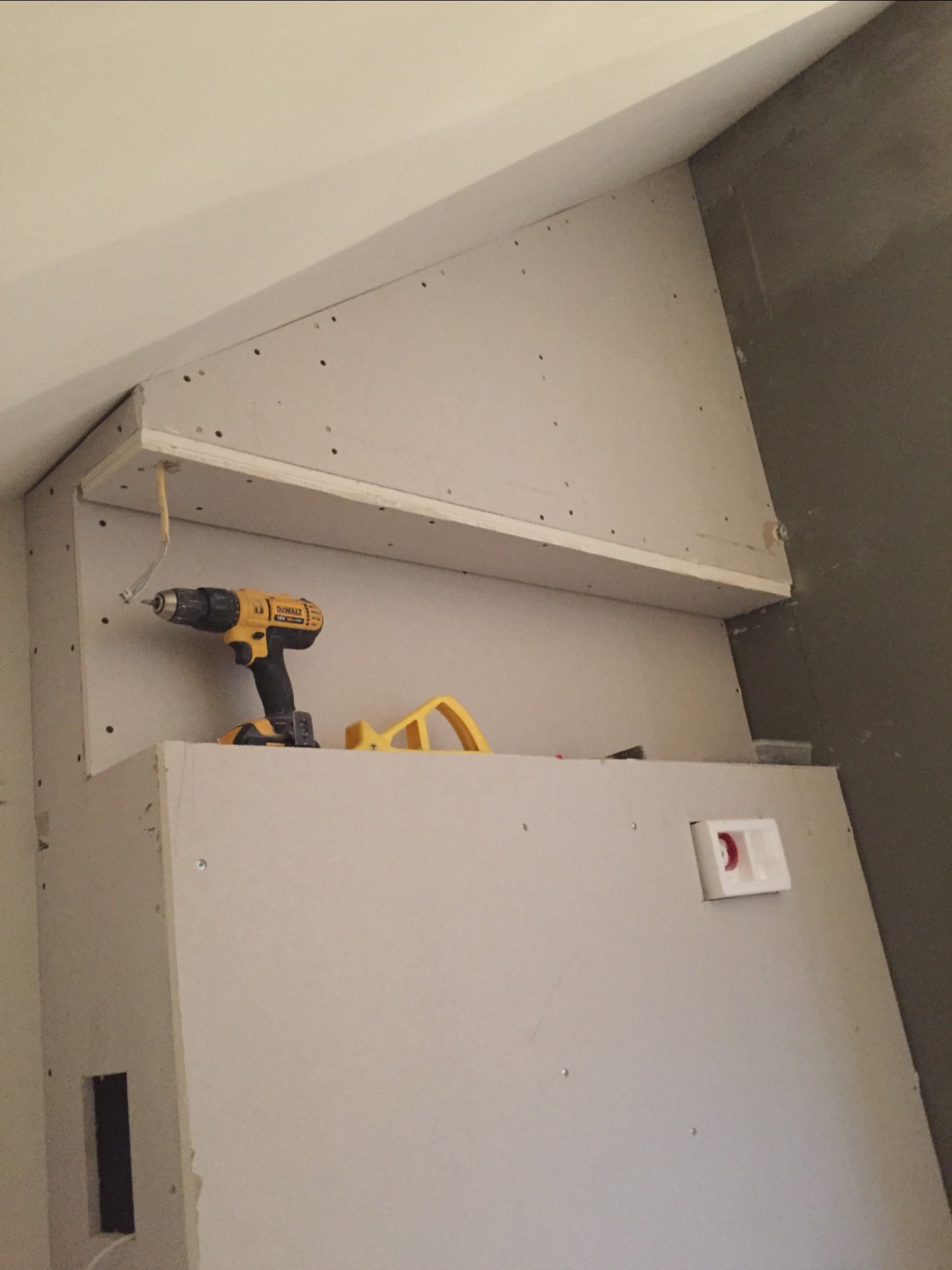 Montaż zabudowy z płyt gipsowo-kartonowych z półką, widoczna wkrętarka DeWalt, otwór instalacyjny i wystający przewód elektryczny.