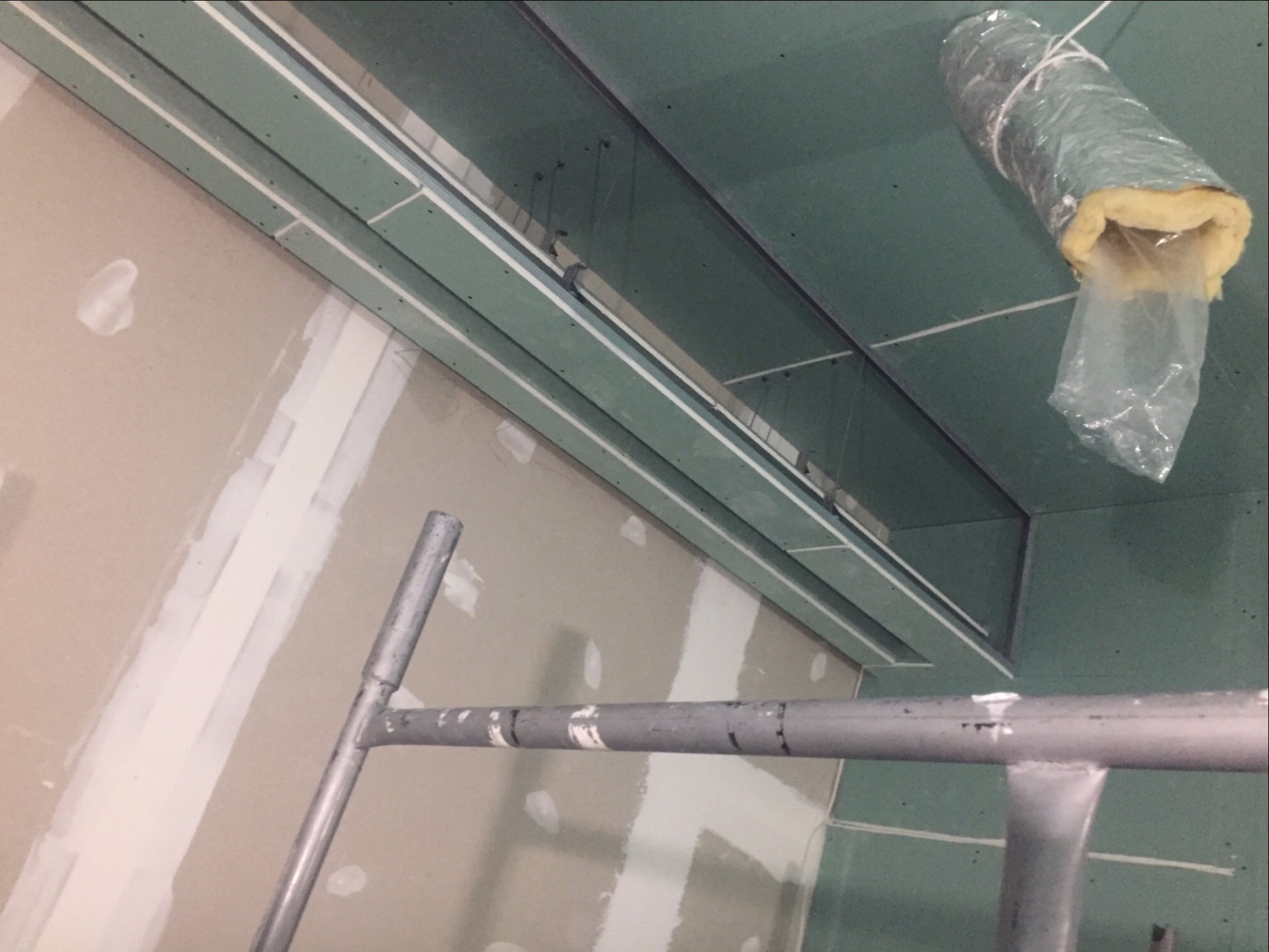 Montaż płyt kartonowo-gipsowych na suficie podwieszanym, widoczne profile, izolacja w folii i fragment rusztowania.