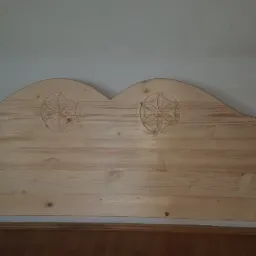 Surowe drewniane wezgłowie łóżka z wyciętymi wzorami kwiatowymi, widoczne śruby montażowe.