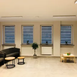 Jasne wnętrze z trzema oknami wyposażonymi w czarno-białe rolety dzień i noc w Witkowie, sofa, stoliki kawowe i stolik dla dzieci z zabawkami.