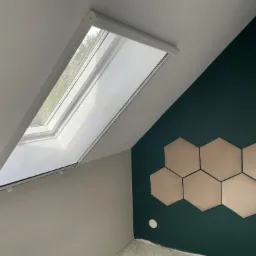 Okno dachowe z zamontowaną siatką przeciw owadom, widok z wnętrza, ściana w kolorze butelkowej zieleni z dekoracyjnymi heksagonami.