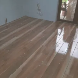 Świeżo ułożona, błyszcząca podłoga z płytek imitujących drewno, z plastikowymi krzyżykami dystansowymi, widoczne gniazdka elektryczne na ścianie w tle.