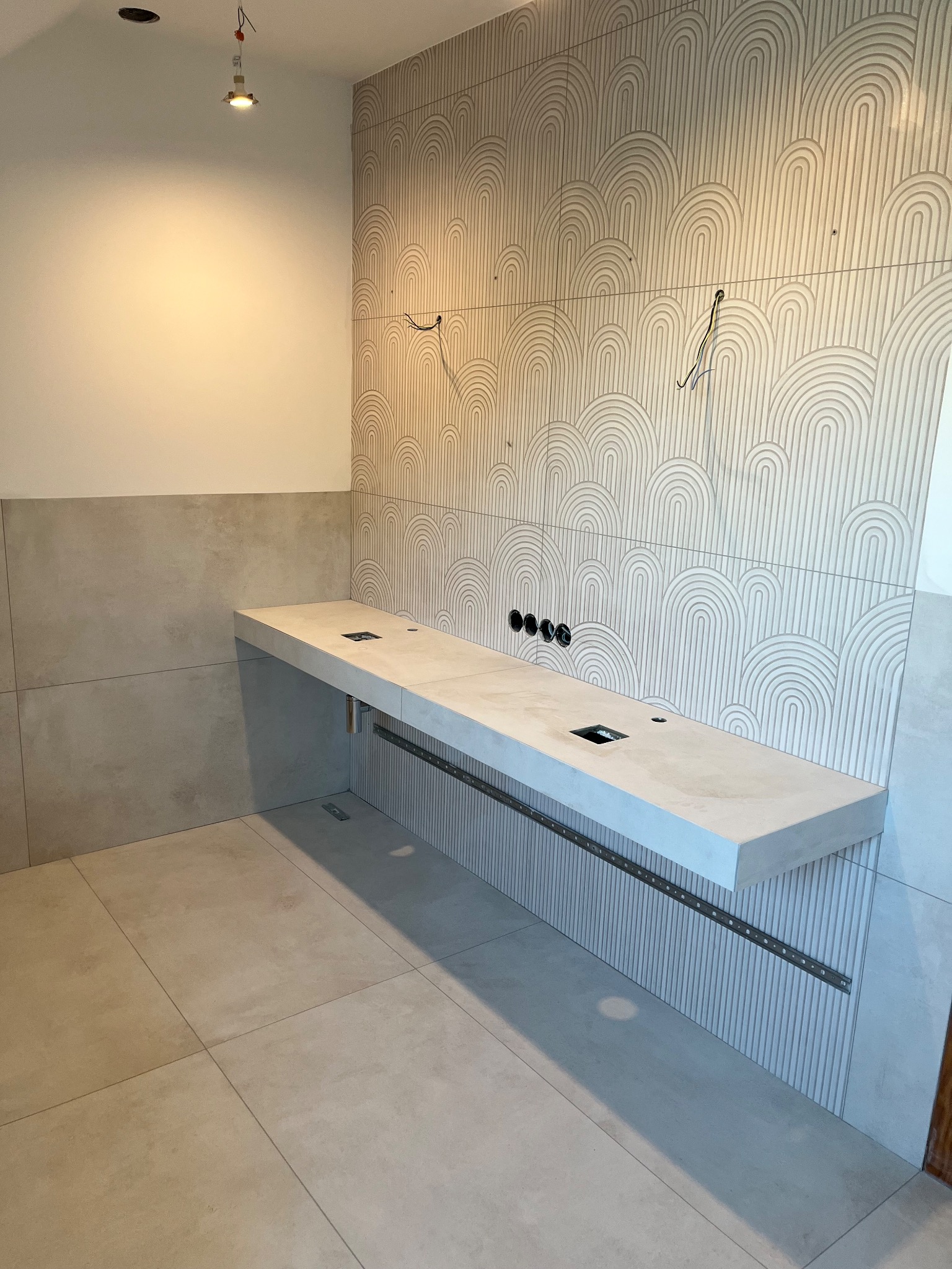 Wykończona łazienka z beżowymi płytkami o wzorze łuków na ścianie, podwieszanym blatem i widocznymi instalacjami elektrycznymi. Minimalistyczny design.