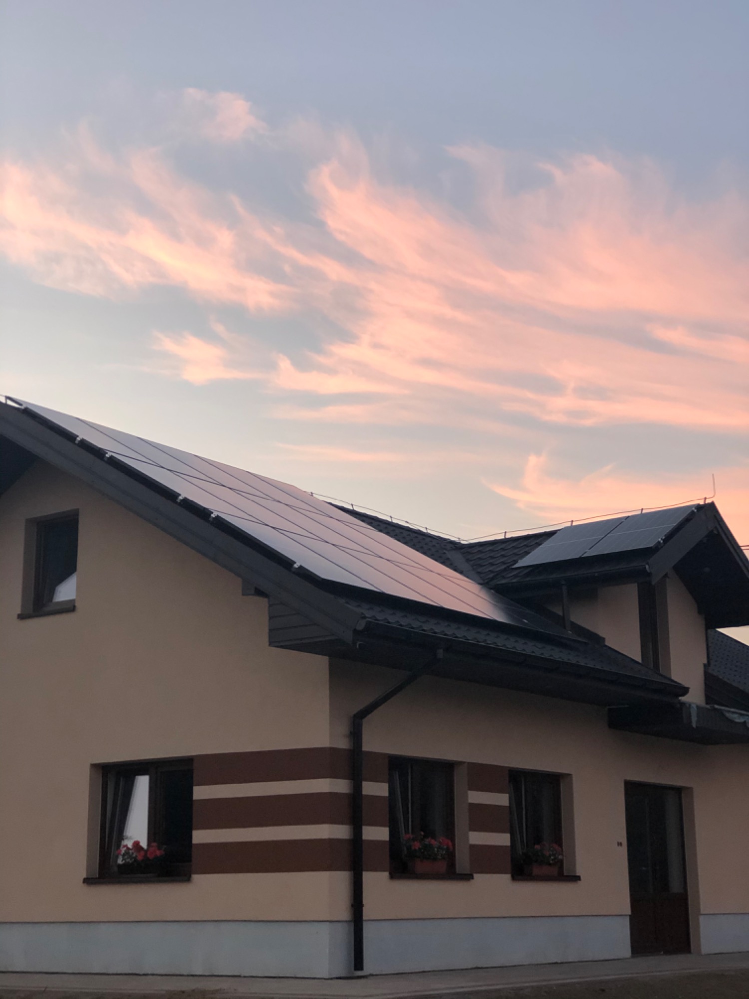 Dom jednorodzinny z panelami słonecznymi na dachu, sfotografowany o zmierzchu, z różowymi chmurami na niebie.